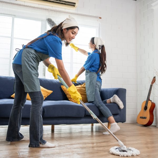 Asian young woman cleaner team cleaning indoors in living room at home. Two beautiful girl housewife housekeeper cleaner feeling happy and relax, enjoy housekeeping housework or chores in house.